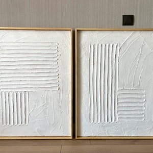 Puede incluir: Dos lienzos blancos texturizados con l&iacute;neas en relieve en un patr&oacute;n geom&eacute;trico, enmarcados en madera natural.