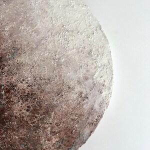 May include: A round, textured, white and brown abstract painting with a gradient effect. The painting has a rough, almost sandy texture.