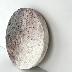 May include: A round, white, textured ceramic wall art piece with a gradient of gray and brown.