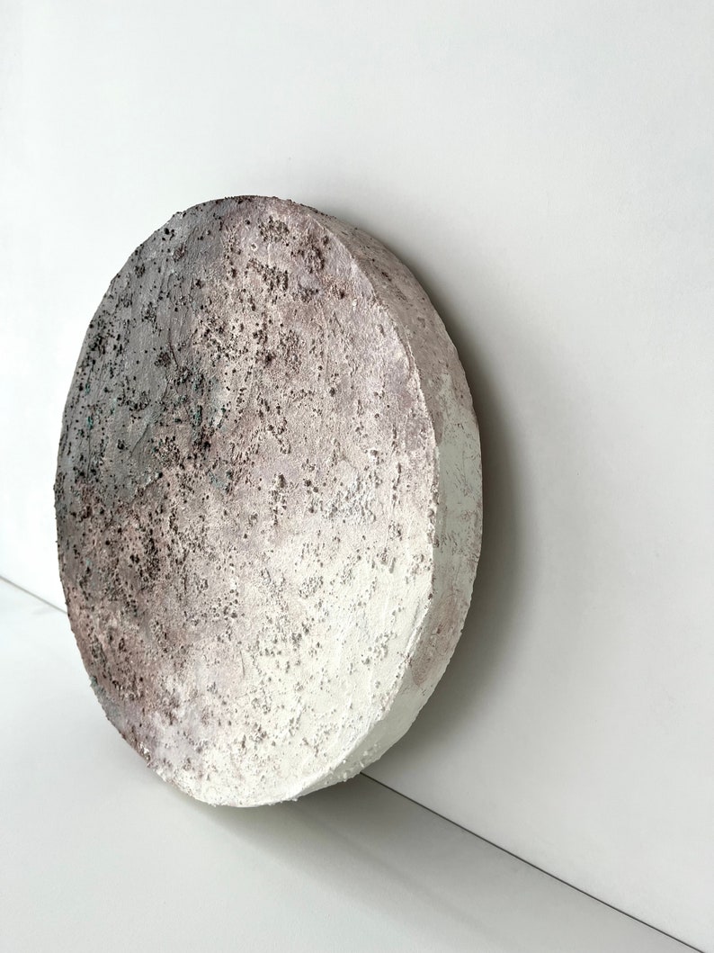 May include: A round, white, textured ceramic wall art piece with a gradient of gray and brown.