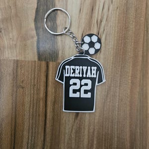May include: Black and white soccer jersey keychain with the name "Deriyah" and the number "22" on the back. The keychain also features a small soccer ball charm.