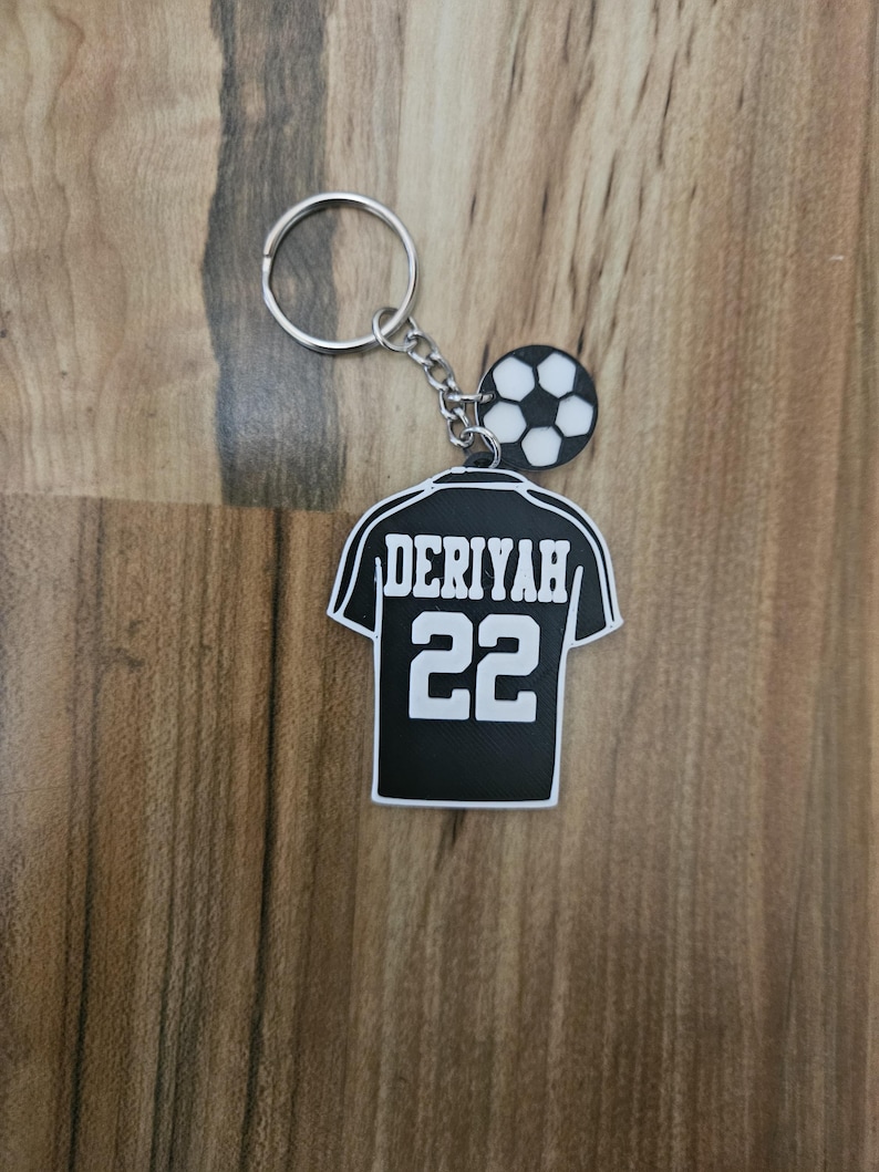 May include: Black and white soccer jersey keychain with the name "Deriyah" and the number "22" on the back. The keychain also features a small soccer ball charm.