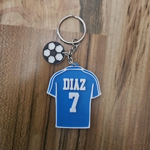 May include: Blue soccer jersey keychain with the name "DIAZ" and the number "7" printed on the back. A small black and white soccer ball charm is attached to the keychain.