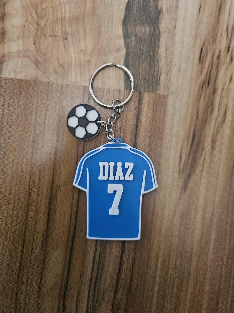 May include: Blue soccer jersey keychain with the name "DIAZ" and the number "7" printed on the back. A small black and white soccer ball charm is attached to the keychain.