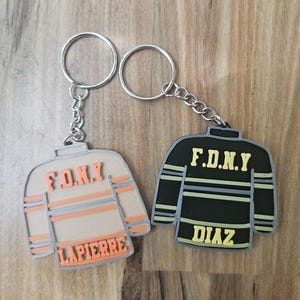 May include: Two firefighter-themed keychains. One is tan with orange accents and the text "F.D.N.Y" and "LAPIERRE". The other is black with yellow accents and the text "F.D.N.Y" and "DIAZ". Both have silver key rings.