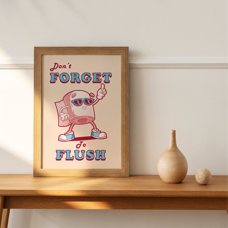 May include: A framed print with a cartoon toilet paper roll wearing sunglasses and saying "Don't forget to flush". The background is a light beige color.