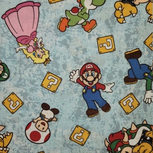 Może przedstawiać: Jasnoniebieska tkanina z kolorowymi postaciami z kresk&oacute;wek z serii gier wideo Super Mario. Projekt zawiera Mario, księżniczkę Peach, Yoshiego, Bowsera i bloki ze znakiem zapytania.
