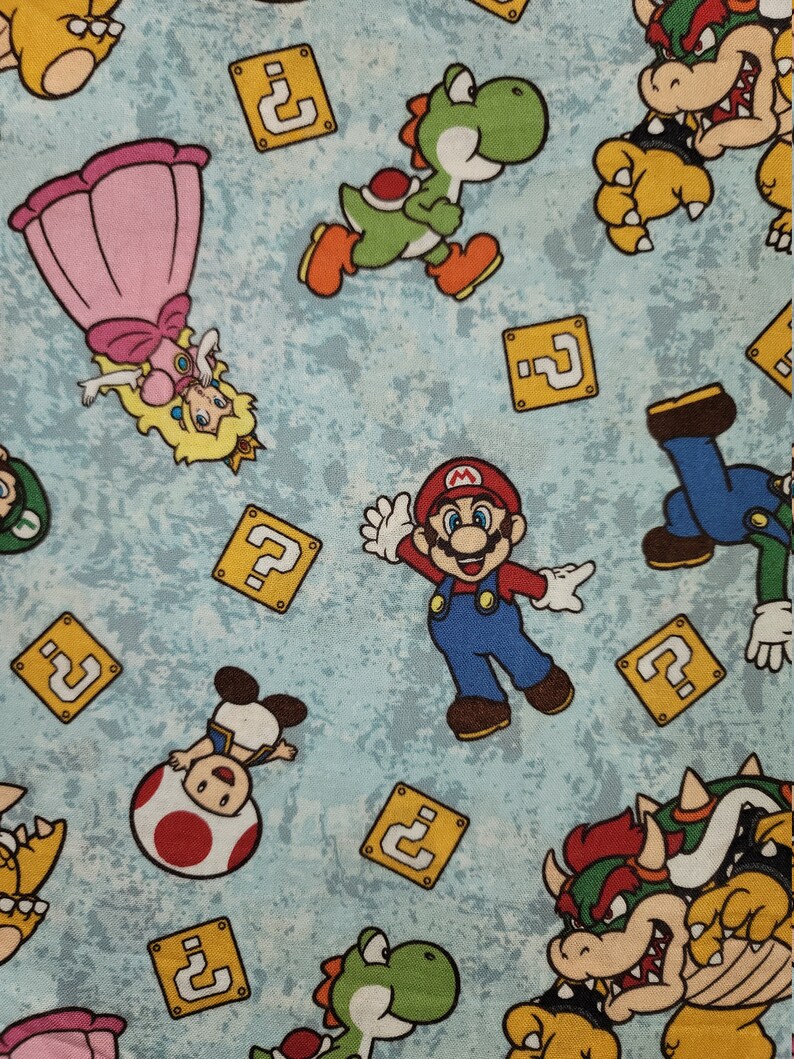 Może przedstawiać: Jasnoniebieska tkanina z kolorowymi postaciami z kresk&oacute;wek z serii gier wideo Super Mario. Projekt zawiera Mario, księżniczkę Peach, Yoshiego, Bowsera i bloki ze znakiem zapytania.