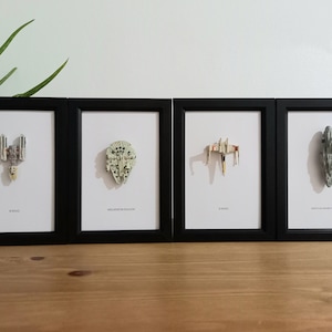 May include: Four framed prints featuring iconic spaceships from a science fiction franchise. The prints are in black frames with white backgrounds. The ships include a Y-wing, Millennium Falcon, X-wing, and a ship with the text "Slave I".