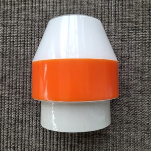 May include: A white and orange ceramic lampshade with a rounded top and a cylindrical base.