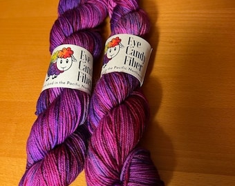 May include: Two skeins of purple and pink yarn with a white sheep logo and the text "Eye Candy Fiber" on the label.
