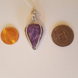 May include: A silver wire wrapped pendant featuring a purple and gray stone. The pendant is about the size of a US quarter.