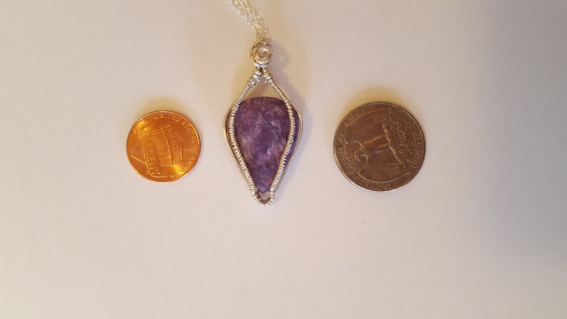 May include: A silver wire wrapped pendant featuring a purple and gray stone. The pendant is about the size of a US quarter.