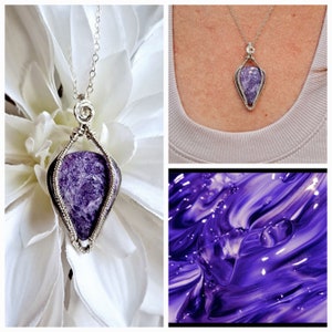 May include: A silver wire wrapped pendant featuring a purple amethyst stone. The pendant is hanging from a silver chain and is displayed on a white flower.