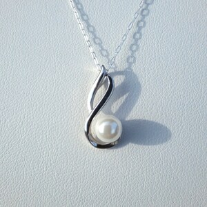 May include: A silver necklace with a pearl pendant. The pendant is shaped like a sideways figure eight.