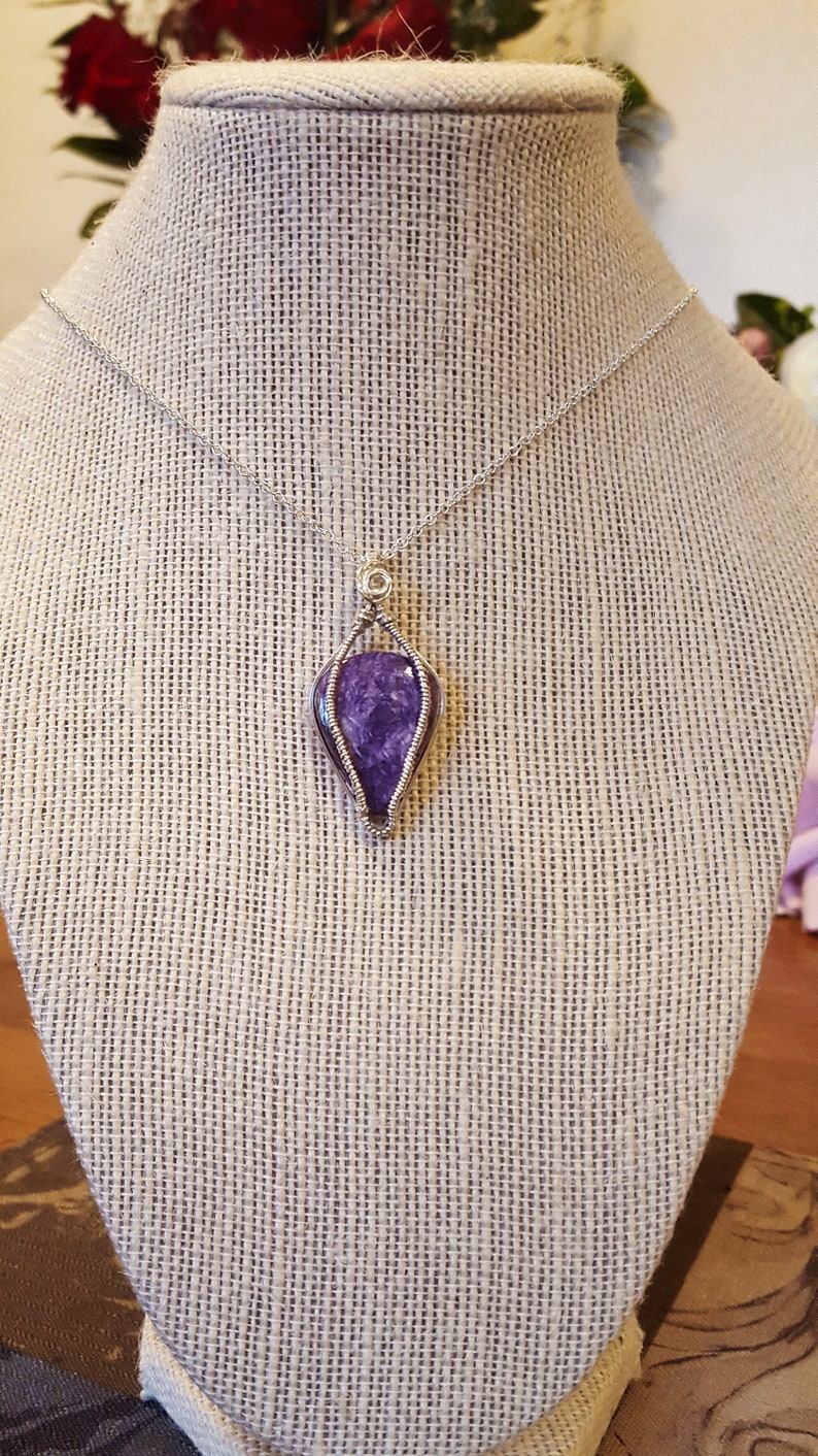 May include: A silver chain necklace with a purple gemstone pendant wrapped in silver wire.