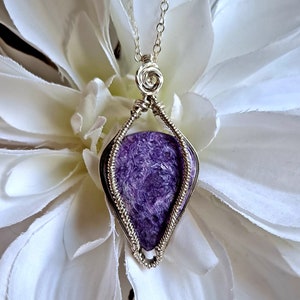 May include: A silver wire wrapped pendant featuring a purple amethyst stone. The pendant is hanging from a silver chain.