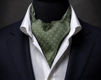 Könnte beinhalten: Ein olivgrünes Seiden-Ascot mit einem sich wiederholenden Muster aus kleinen weißen Blumenmotiven, das in ein weißes Hemd mit Kragen unter einem dunkelblauen Blazer gesteckt ist. Das Ascot ist in traditioneller Weise um den Hals gebunden.