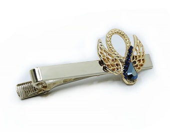 May include: A gold-tone hair clip with a decorative swan design. The swan has blue crystal accents and a teardrop-shaped blue crystal in the center.