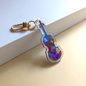 May include: A gold key chain with a clear acrylic charm featuring a colorful violin with a floral design.