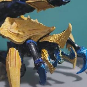 Op de afbeelding: Een geschilderd miniatuurfiguur van een schorpioenachtig wezen met een gesegmenteerd lichaam. Het wezen heeft een donkerblauw en zwart hoofdlichaam met felgele pantserplaten op de rug en poten, en scherpe blauwe klauwen en scharen.