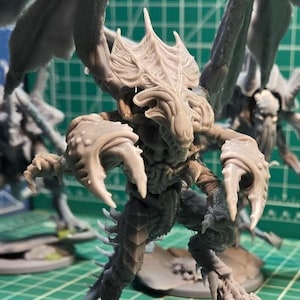May include: A collection of unpainted grey resin miniature figures featuring winged, insectoid creatures with sharp claws and segmented bodies. Each figure stands on a circular base, with the central creature posed on a rock next to a small egg.