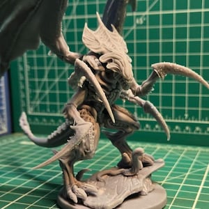 May include: A grey, unpainted resin miniature of a winged creature with sharp, elongated claws and a segmented exoskeleton. The figure stands on a circular base, featuring a detailed head crest and large, leathery wings spread wide in a dynamic pose.