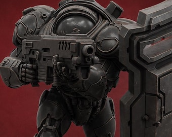 May include: A dark gray armored figure, holding a rifle and a shield, stands on a black circular base. The figure has a detailed, mechanical design, with visible joints and panels. The background is a solid, deep red.