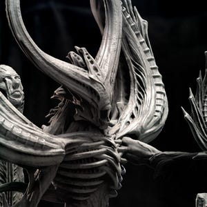 May include: A series of gray sculptures, each depicting a skeletal figure with elaborate headgear and outstretched arms. The sculptures are approximately 130mm tall and are labeled "GIGER MONSTER TRIBUTE".