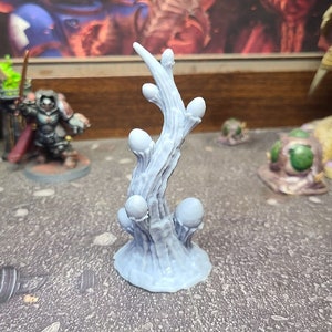 Puede incluir: Una miniatura gris de una planta impresa en 3D con un tallo retorcido y múltiples crecimientos redondos y bulbosos. La planta se coloca sobre un fondo gris texturizado.