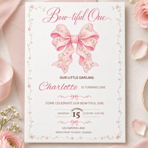 May include: A white birthday invitation card featuring a large pink bow with floral patterns, the text Bow-tiful One, Our Little Darling Charlotte is turning one, Come celebrate our bow-tiful girl, Saturday November 15, 2:00 PM-5:00 PM, 123 Garden Lane, RSVP to Daisy 0123456.