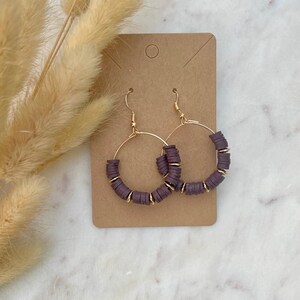 May include: A pair of gold hoop earrings with a row of dark purple beads around each hoop.