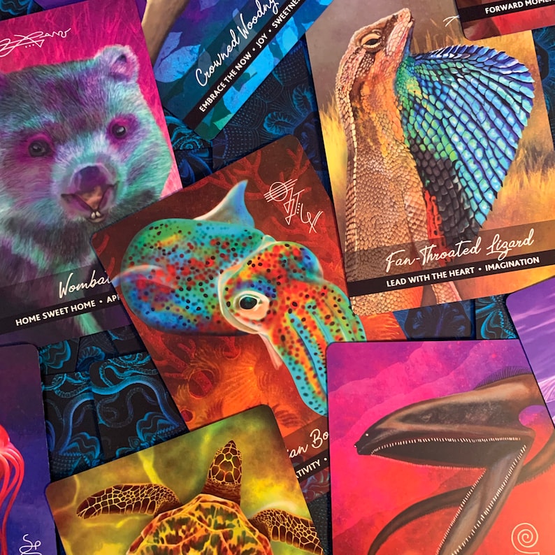 Peut inclure: Un jeu de cartes d'oracle color&eacute;es repr&eacute;sentant divers animaux et sc&egrave;nes de nature. Les cartes ont un fond sombre avec des couleurs vives et des illustrations d&eacute;taill&eacute;es. Les cartes comprennent des images d'un wombat, d'un calmar, d'un l&eacute;zard, d'une tortue et d'une cr&eacute;ature marine.