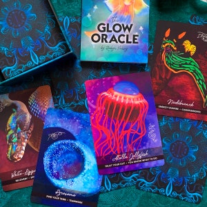 Peut inclure: Un jeu de cartes d'oracle avec des illustrations color&eacute;es de cr&eacute;atures marines. Les cartes pr&eacute;sentent le texte "The Glow Oracle by Robyn Voisey" et comprennent des noms comme "Atolla Jellyfish", "White-Lippe", "Pyrosome" et "Nudibranch".