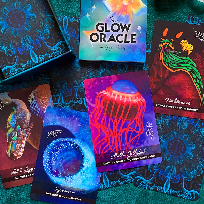 Peut inclure: Un jeu de cartes d'oracle avec des illustrations color&eacute;es de cr&eacute;atures marines. Les cartes pr&eacute;sentent le texte "The Glow Oracle by Robyn Voisey" et comprennent des noms comme "Atolla Jellyfish", "White-Lippe", "Pyrosome" et "Nudibranch".