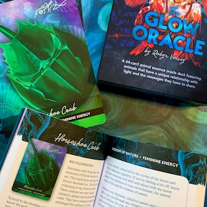 Peut inclure: Gros plan sur une carte du jeu d'oracle Glow Oracle, repr&eacute;sentant un crabe fer &agrave; cheval avec une lueur biofluorescente. Le titre de la carte est "Horseshoe Crab" et le texte indique "Wisdom of Nature - Feminine Energy".