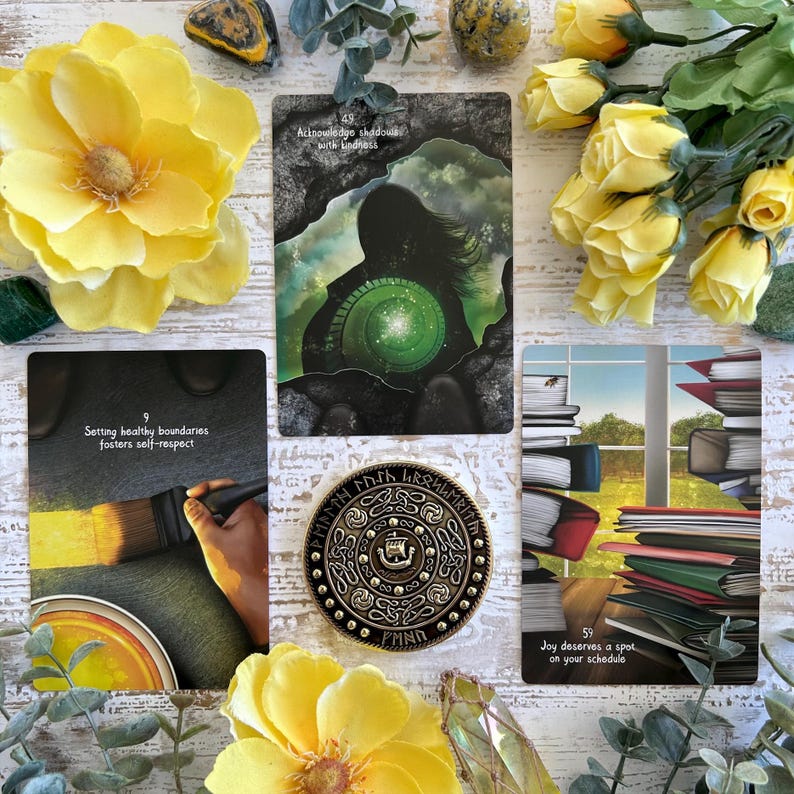 May include: Four oracle cards with colorful illustrations and text. The cards are laid out on a white wooden surface with yellow flowers. The text on the cards reads: "Setting healthy boundaries fosters self-respect", "Acknowledge shadows with kindness", "Joy deserves a spot on your schedule", and a circular card with a design and text in a foreign language.