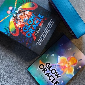 Peut inclure: Deux bo&icirc;tes du jeu de cartes oracle Glow Oracle avec des cartes d'oracle d'essence animale. Les bo&icirc;tes sont noires avec des illustrations d'animaux color&eacute;s et le texte "Glow Oracle" et "par Robyn Voisey".