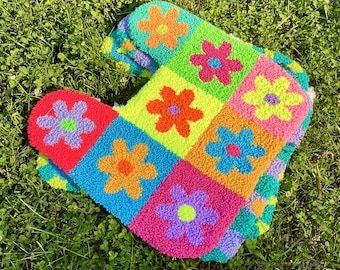 May include: A colorful, handmade rug featuring a patchwork design of vibrant squares. Each square showcases a different color and a flower in the center. The rug's bright colors include pink, orange, blue, green, and yellow, creating a cheerful aesthetic.