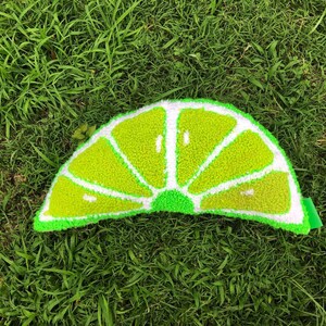 May include: A green lime slice shaped rug with a white center. The rug is made of a fluffy, textured material and is sitting on a green grassy surface.