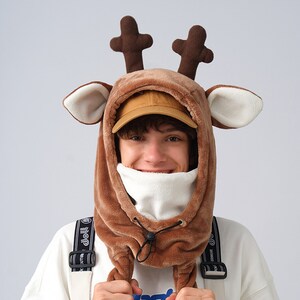May include: A brown plush reindeer hooded hat with a white fleece lining and a brown drawstring. The hat has large ears and antlers.