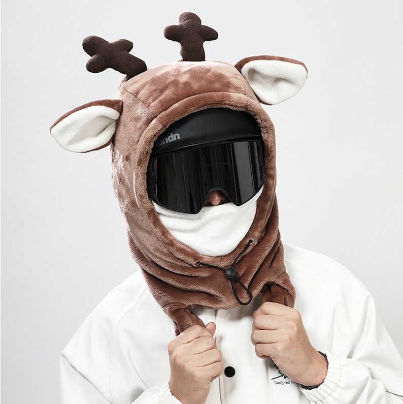 May include: A brown fleece ski mask with reindeer ears and a black ski goggle. The mask has a drawstring to tighten it around the neck.