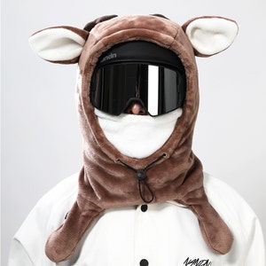 May include: A brown fleece ski mask with deer ears and a black ski goggle. The mask has a white fleece lining and a black drawstring.