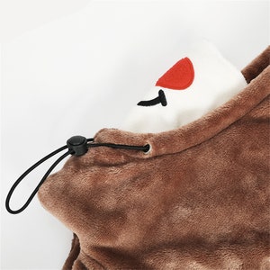May include: Brown fleece hooded neck warmer with a white fleece lining and a red heart embroidered on the lining. The neck warmer has a black drawstring.