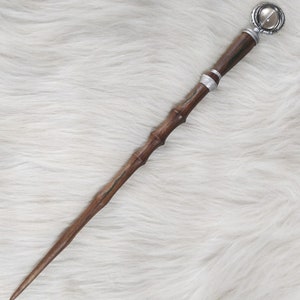 May include: A wooden wand with a dark brown finish, featuring a silver band and a decorative, circular top with a clear stone. The wand has a textured, bamboo-like design and green accents. The wand is approximately 14 inches long.
