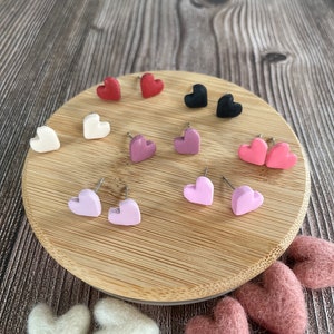 May include: A set of heart-shaped earrings in various colors, including pink, red, white, and black. The earrings are displayed on a wooden surface.