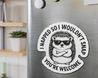 May include: A white magnet featuring a black and white illustration of a hedgehog wearing sunglasses and with crossed arms. The text on the magnet says "I napped so I wouldn't snap, you're welcome."