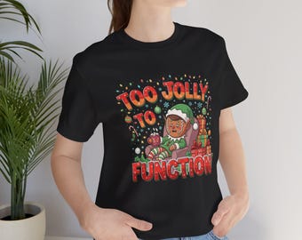 Könnte beinhalten: Schwarzes T-Shirt mit einem Cartoon-Elf-Design und dem Text "TOO JOLLY TO FUNCTION". Der Elf sitzt in einem Stuhl, trägt einen grünen Hut und hält eine Tasse. Festliches Weihnachts-Design mit bunten Details.