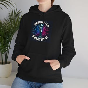 May include: Black hoodie with a front pocket and a drawstring hood. The graphic on the front features a stylized leg with the text "REBUILT FOR GREATNESS" in white, blue, and pink.