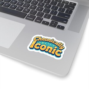 May include: A sticker with the words "Chronically Iconic" in a retro font. The text is yellow with a blue outline and a teal background with star accents. The sticker is on a laptop.